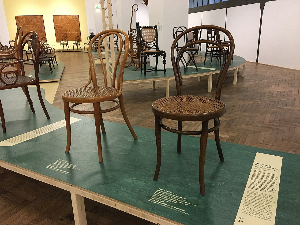 Bentwood chairs stand on exhibition platforms in Vienna; the dark chair at front right is a Thonet No. 14.