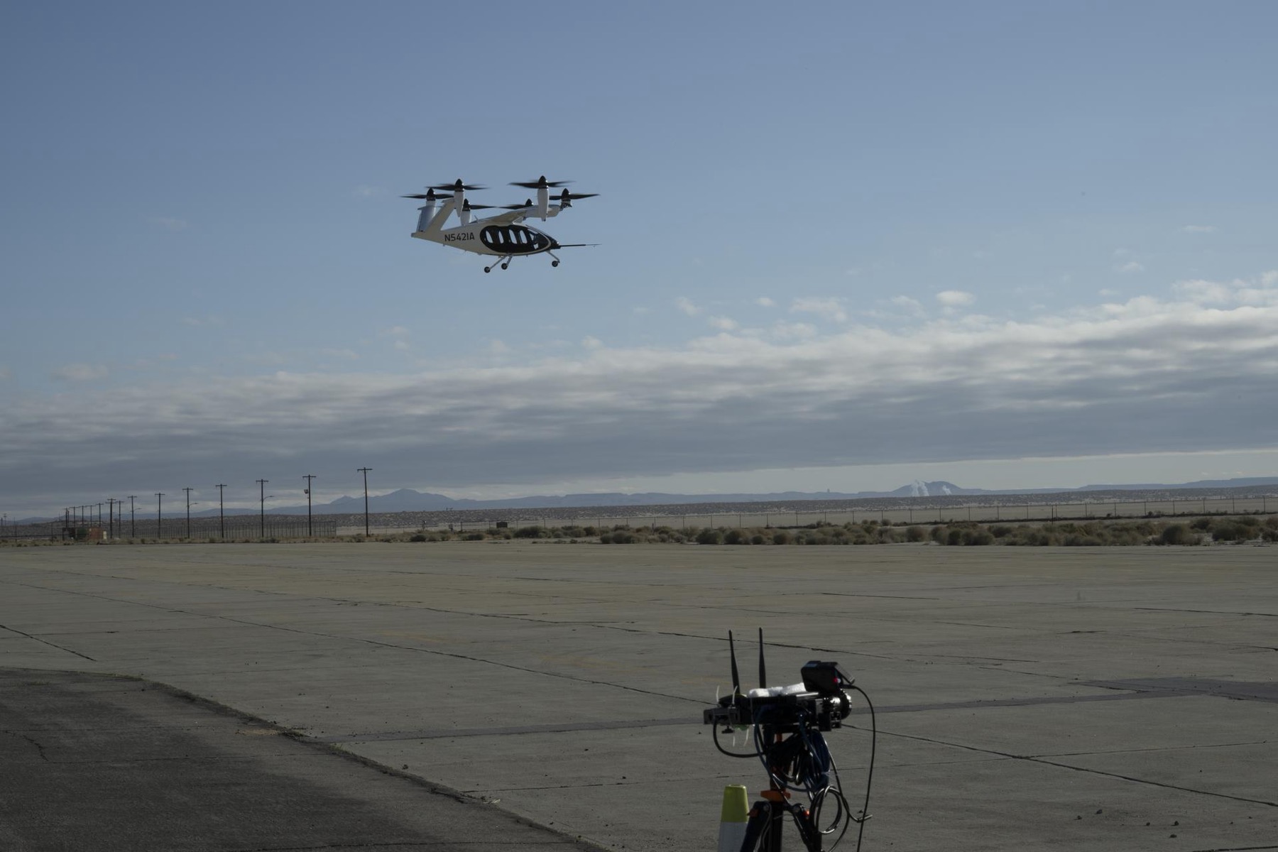 A Joby experimental aircraft hovers above a desert airfield, with a NASA sensing node in the foreground.