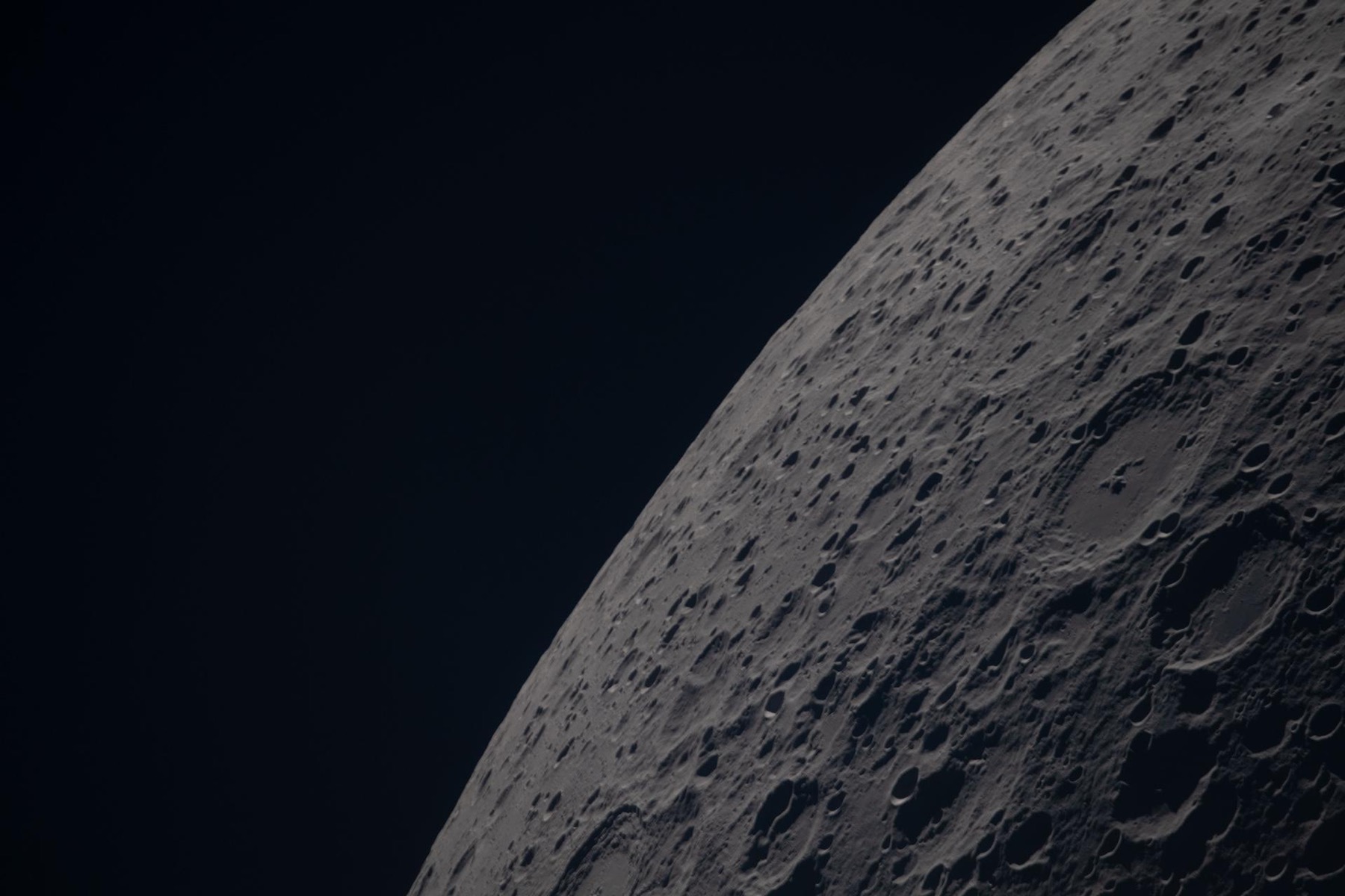 The densely cratered lunar far side fills a diagonal portion of the frame against black space.