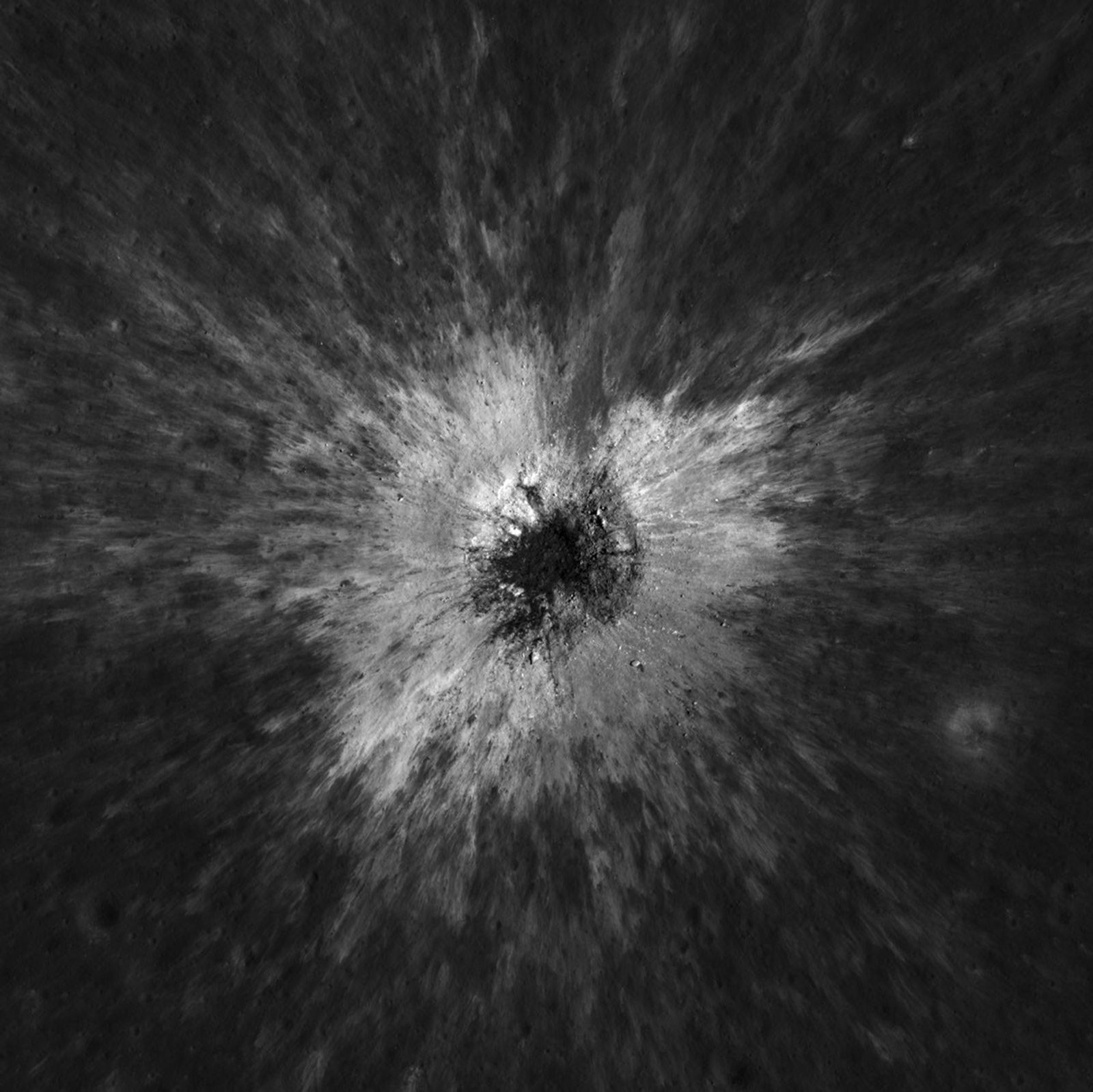 A dark lunar crater surrounded by bright streaks of ejected material.