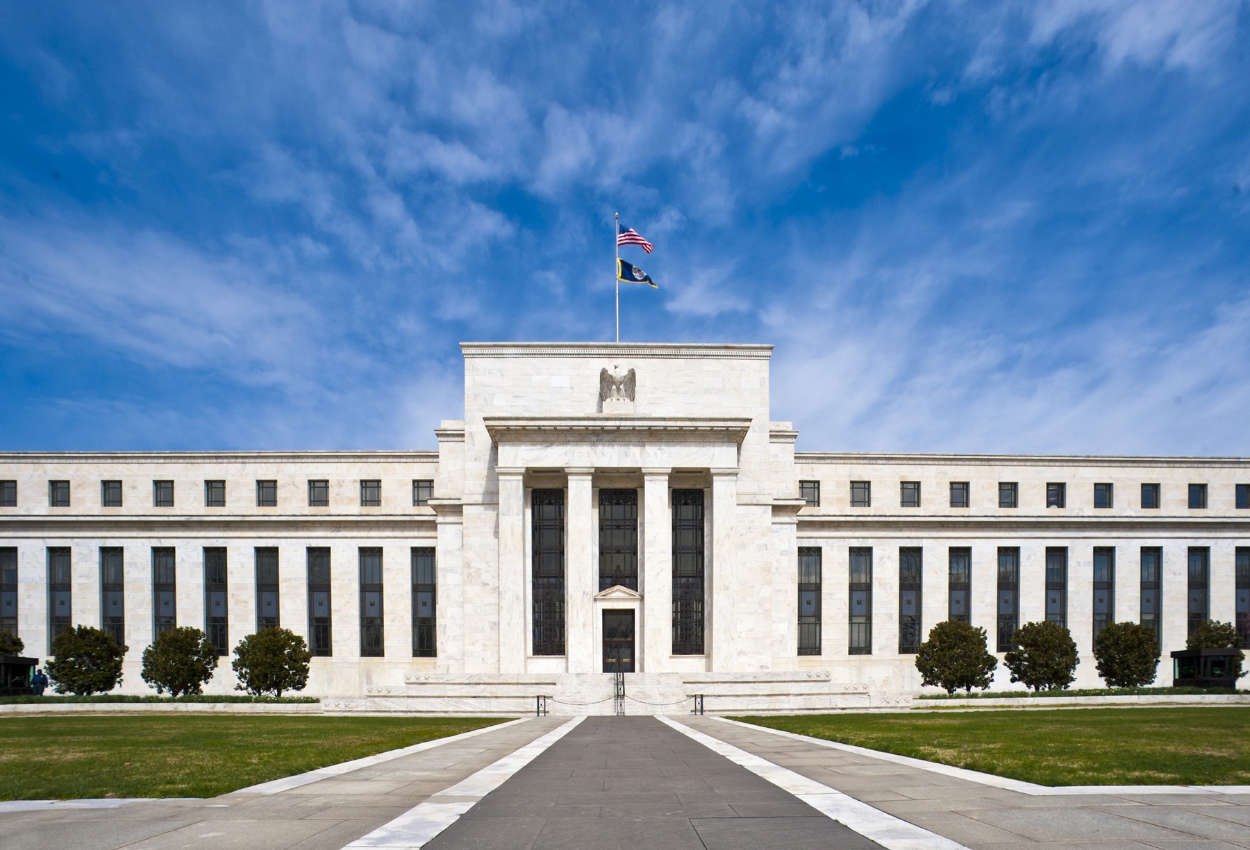 The white stone facade of the Eccles Building beneath an American flag and blue sky.